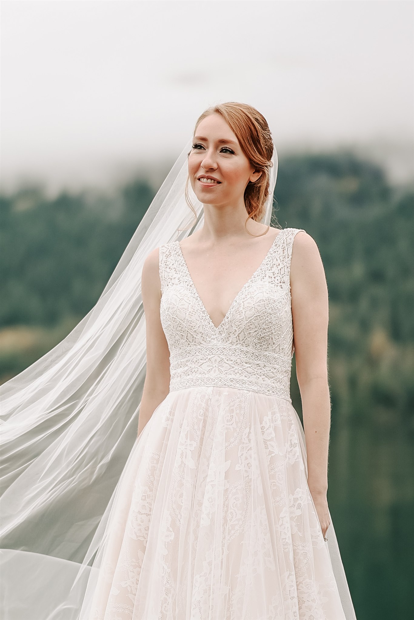 bride standing on a dock with her veil blowing in the wind at her American Creek Lodge Wedding