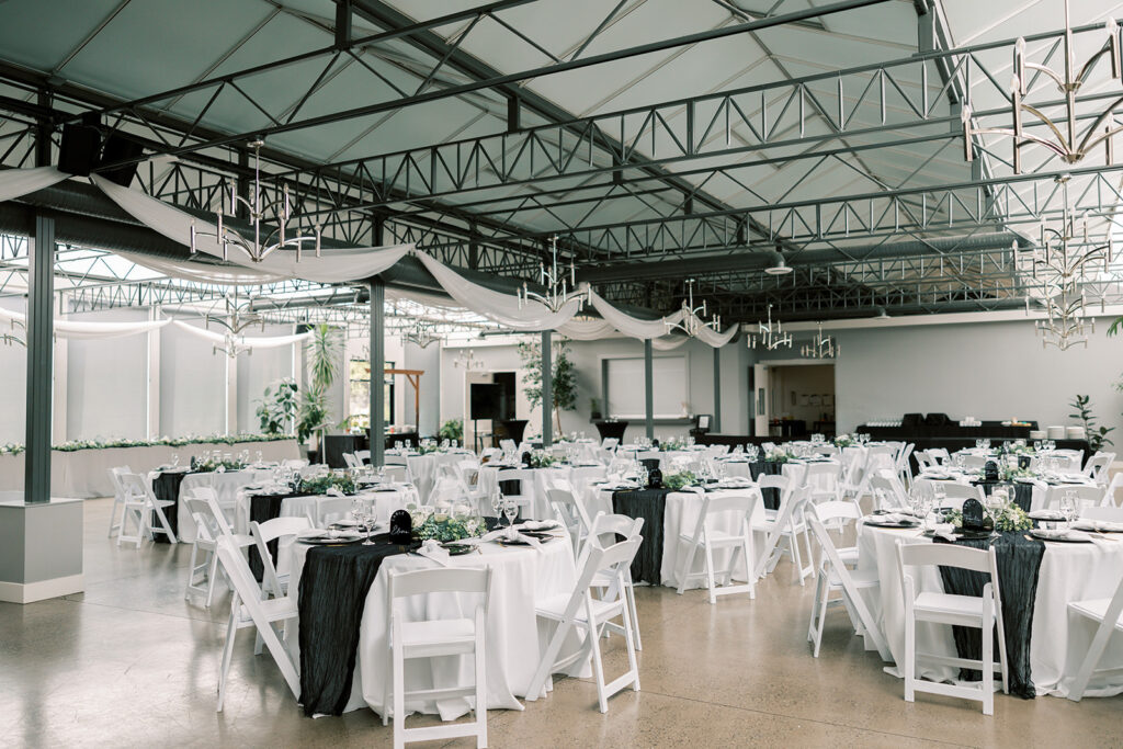 A large reception hall staged for a wedding in a black tie affair with beautiful elegant white chairs