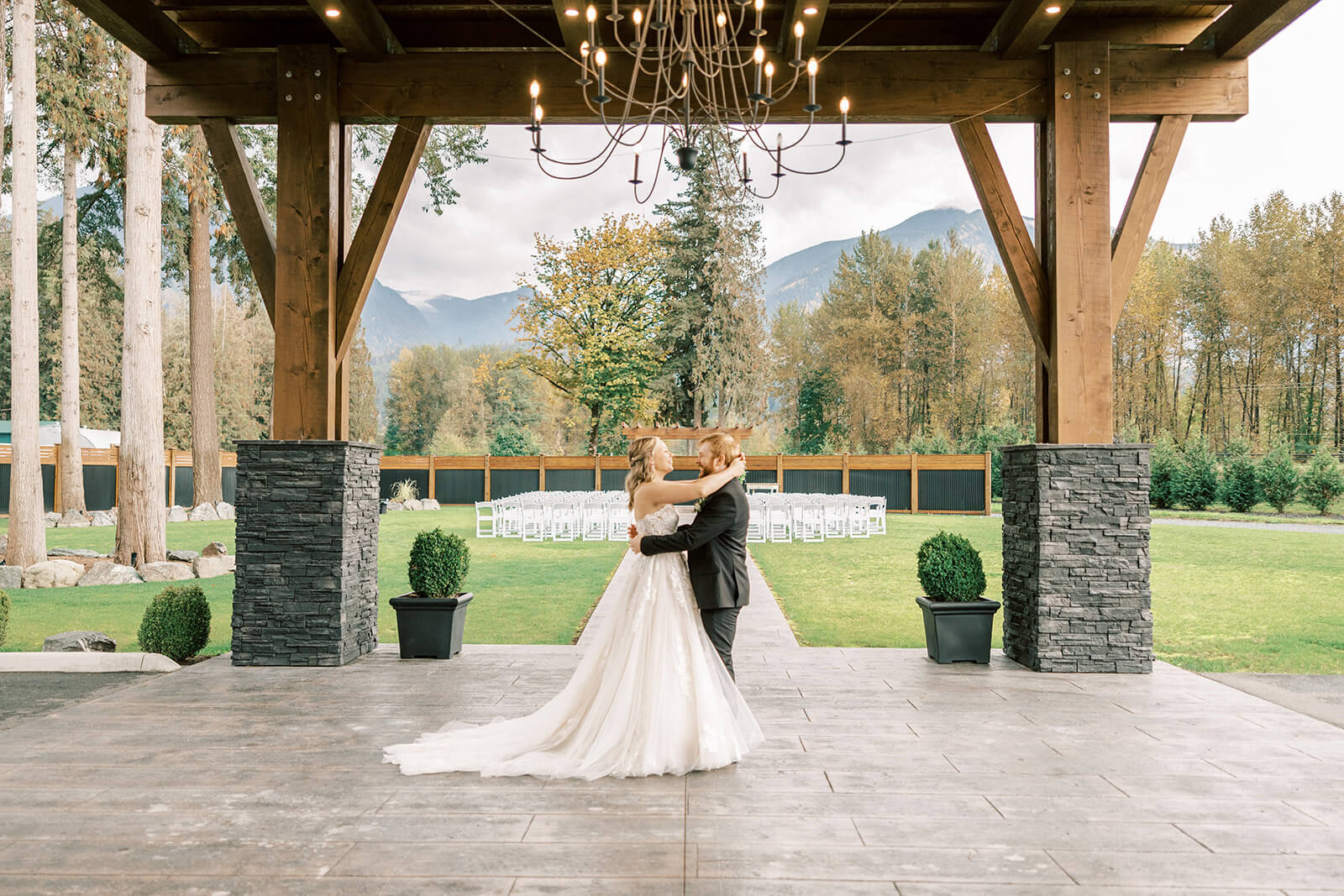 A bride in an elegant ivory wedding dress with a train embracing her groom in the covered space of Bridlewoods Event Center in Chilliwack, BC